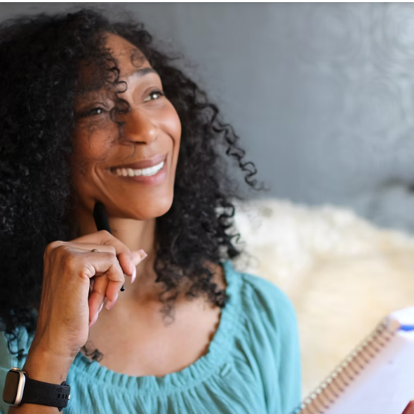 Bleu Winters smiling thoughtfully in a turquoise blouse, holding a pen and notebook